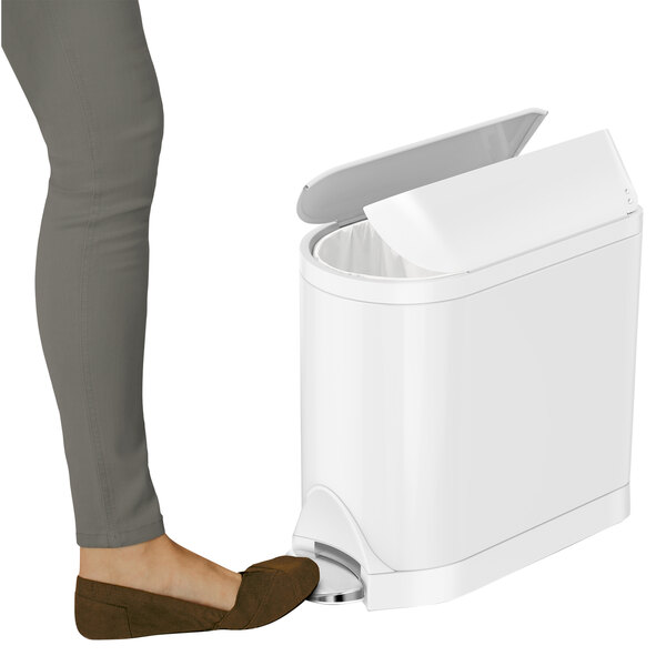 A woman stepping on a white simplehuman rectangular butterfly step-on trash can.