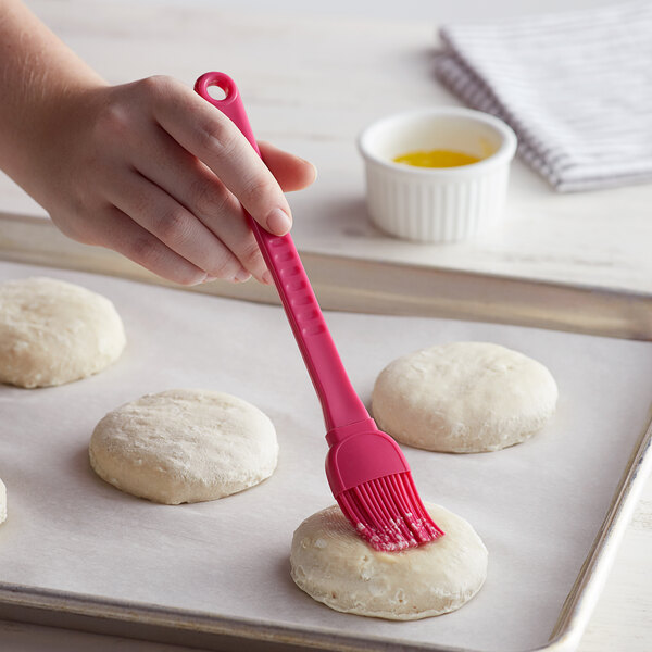 A hand using a Fox Run silicone pastry brush to spread yellow liquid on a white ball of dough.