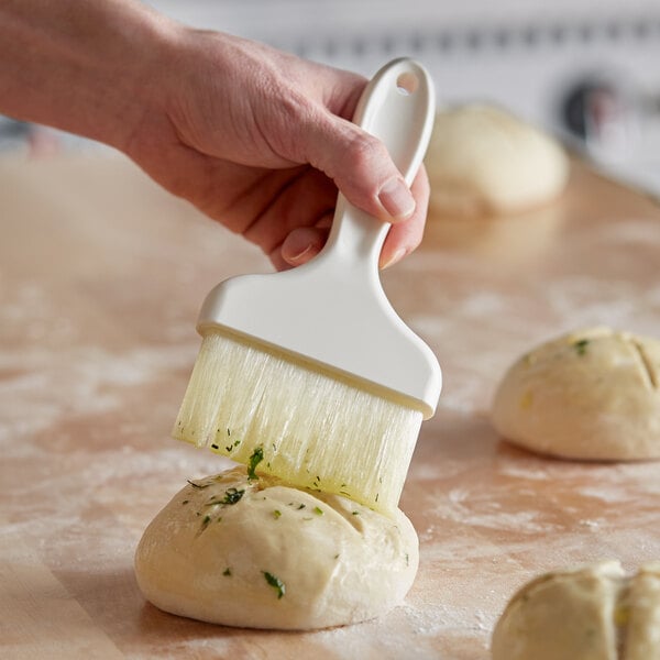 A hand using a Carlisle Sparta Spectrum pastry brush to brush dough.