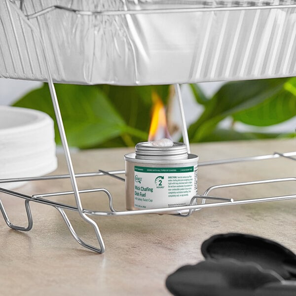 A can of wick chafing dish fuel with a safety twist cap placed under a metal rack supporting an aluminum food tray.