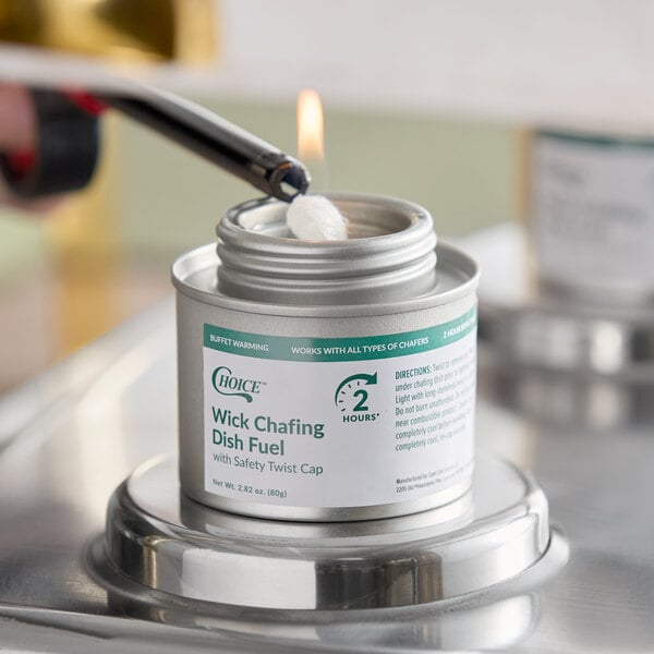 A metal canister labeled 'Wick Chafing Dish Fuel' is being lit with a lighter, with a visible flame on the wick.