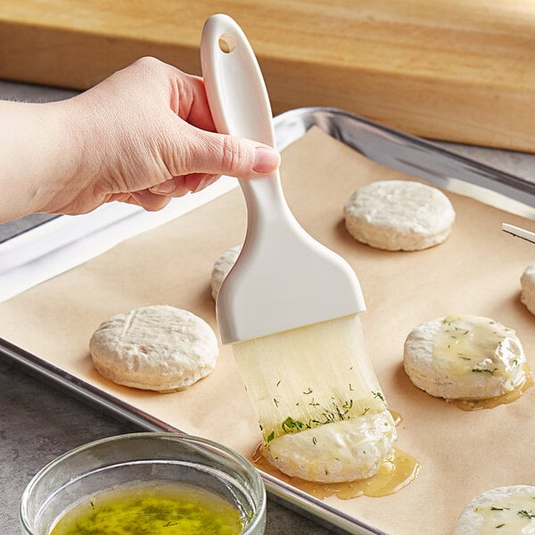 A person using a Carlisle pastry brush to spread yellow liquid over food.