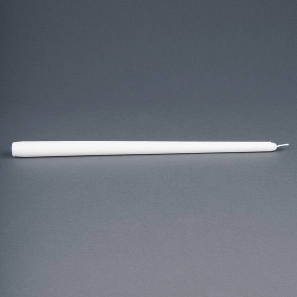 A Will & Baumer white taper candle on a gray surface.