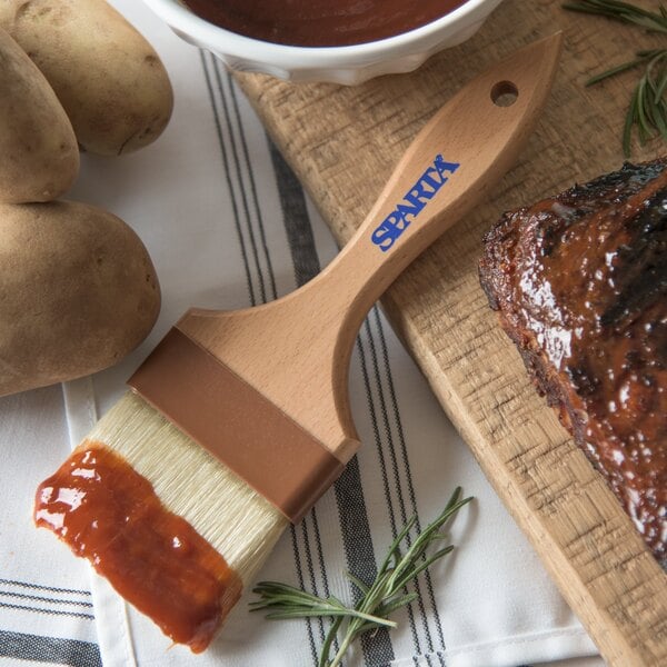 A Carlisle Sparta boar bristle pastry brush next to a bowl of barbecue sauce.