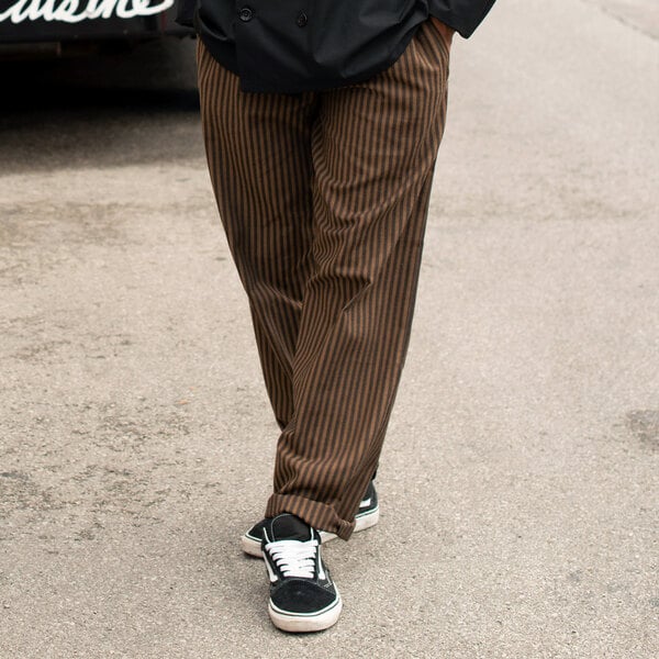A person wearing Uncommon Chef black and copper striped chef pants.
