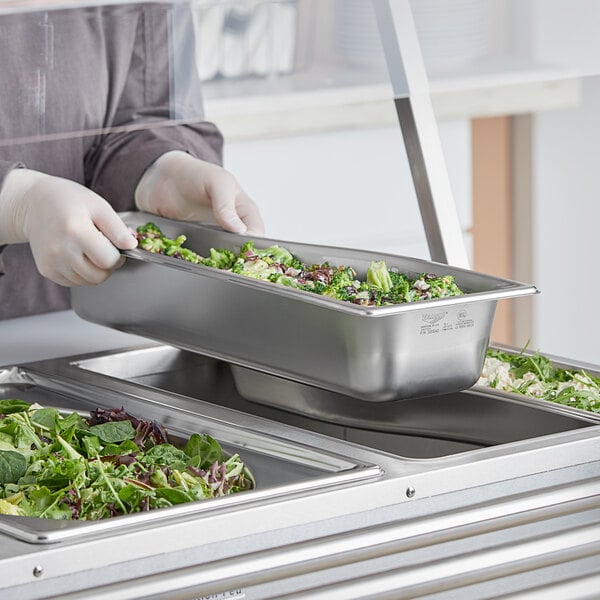 A Vollrath stainless steel long steam table pan with broccoli and onions inside.