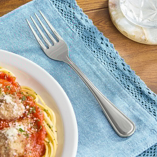 A Oneida New Rim stainless steel dinner fork next to a plate of spaghetti with sauce.