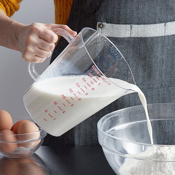 A person using a Carlisle clear polycarbonate measuring cup to pour milk into a bowl of eggs.