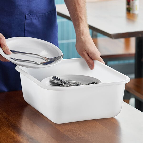 A person holding a Rubbermaid white high density polyethylene food storage box with plates and silverware inside.