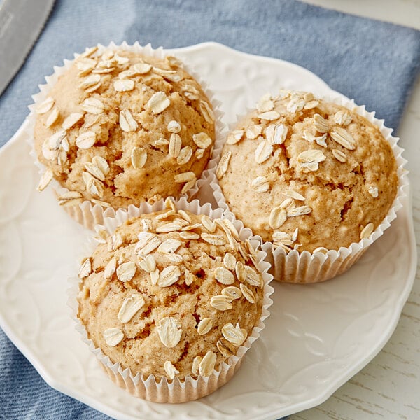 A plate of three Krusteaz Oat Bran muffins with oat flakes on top.