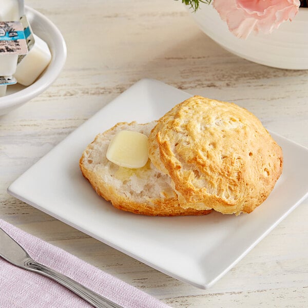 A plate of Krusteaz buttermilk biscuits with butter on a table.