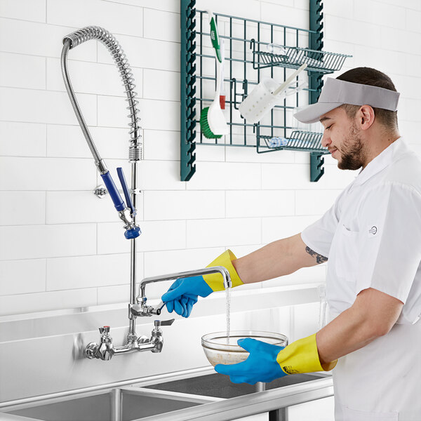 kitchen worker using spray arm to rinse glass bowl