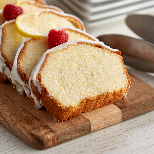 A sliced Krusteaz lemon creme cake with raspberries and lemon slices on a wooden board.