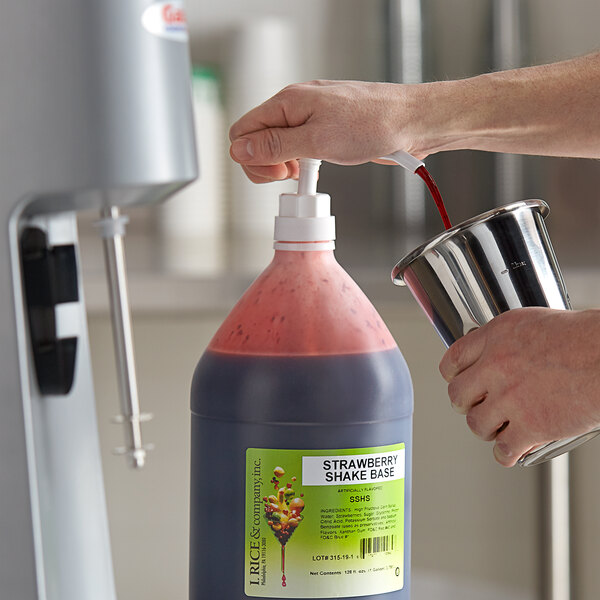A person pouring I. Rice strawberry milkshake base syrup into a container.