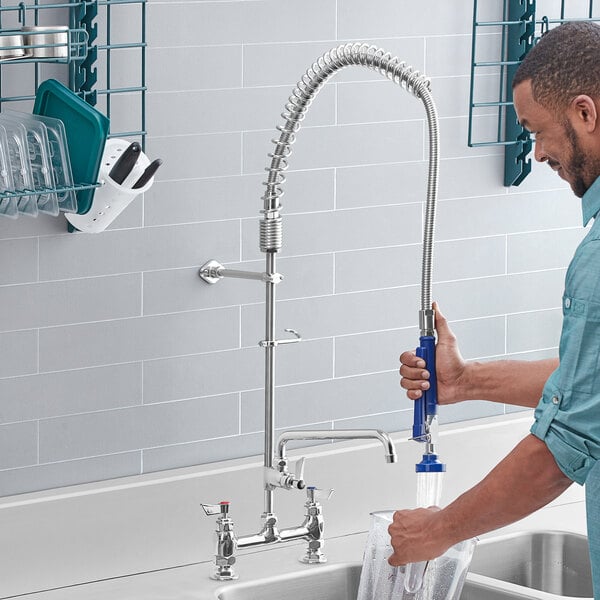 A man using a Waterloo deck-mounted pre-rinse faucet to wash his hands in a professional kitchen sink.