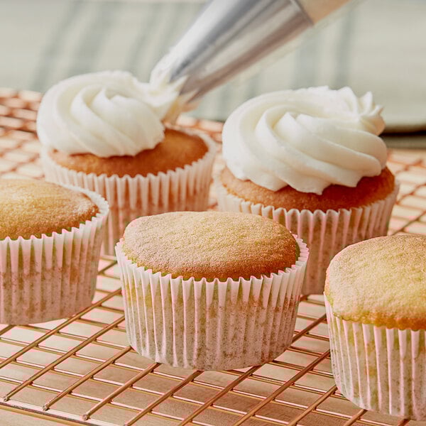 A group of Krusteaz lemon cupcakes with frosting on top in paper wrappers on a cooling rack.
