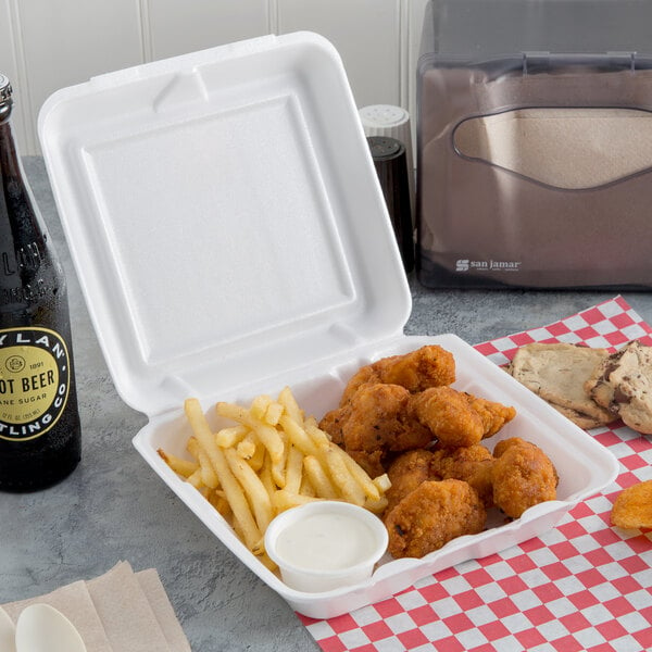 A Dart white foam hinged lid container of chicken and fries next to a bottle of beer.