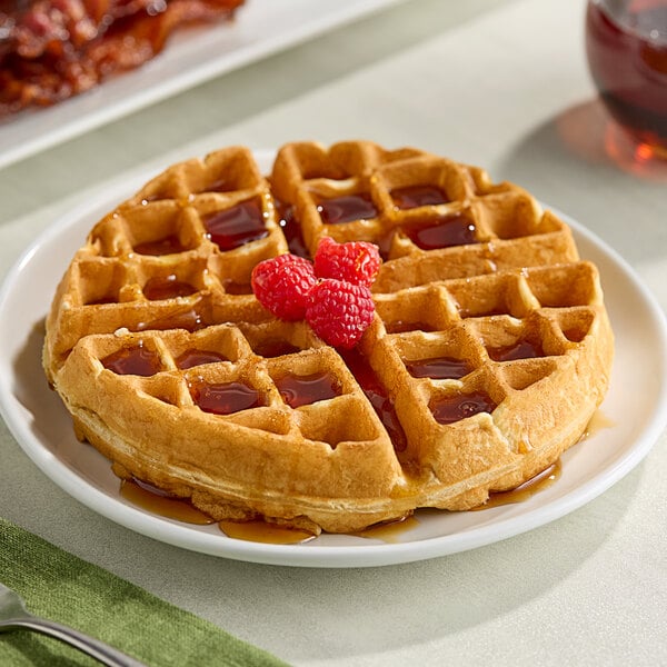 A waffle with raspberries and syrup on top on a white plate.