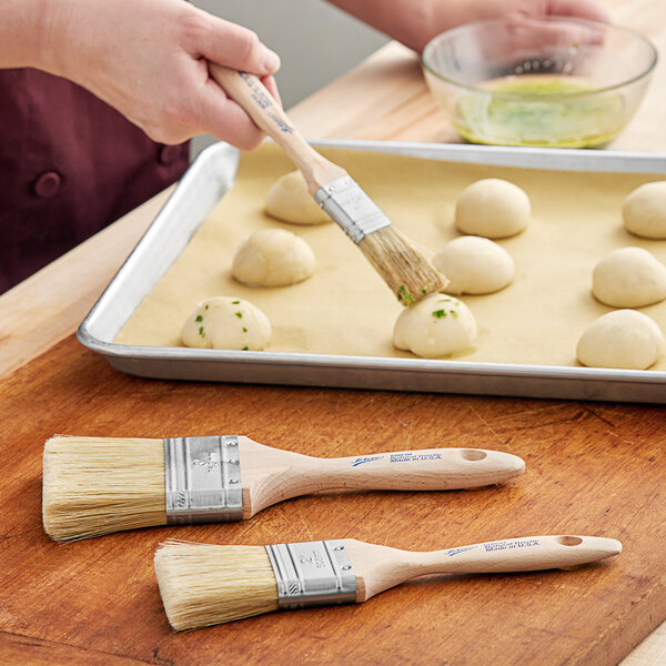 A person using an Ateco boar bristle brush to paint food on a tray.