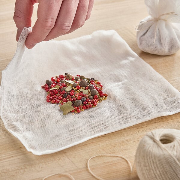 A hand using Monarch Brands bleached cheesecloth to make a tea bag with spices.
