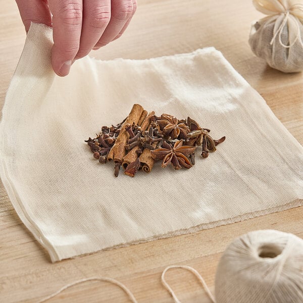 A hand holding Monarch Brands unbleached cheesecloth with a pile of spices.