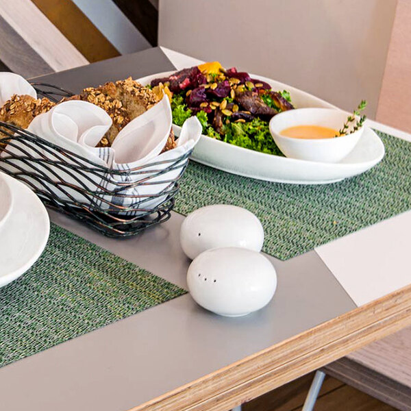 A table with a white plate of food and a white Front of the House Harmony salt and pepper shaker set on it.