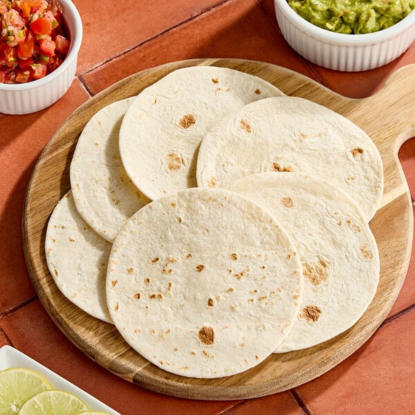 A round wooden board with several small flour tortillas arranged on it.