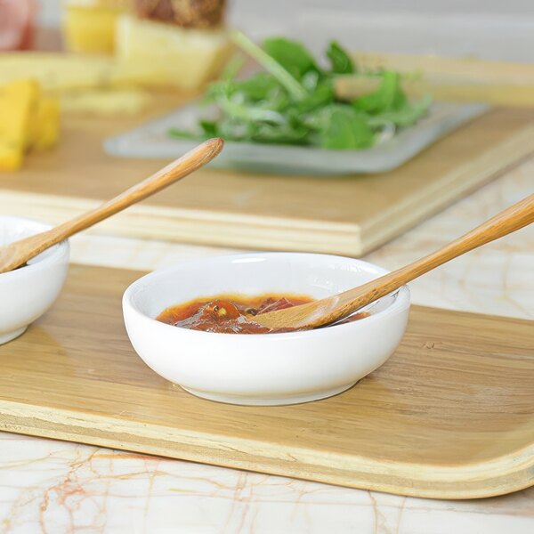 Two bowls of food in Front of the House Harmony bright white porcelain ramekins with wooden spoons on a counter.