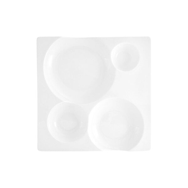 A square white porcelain plate with four round compartments of varying sizes.