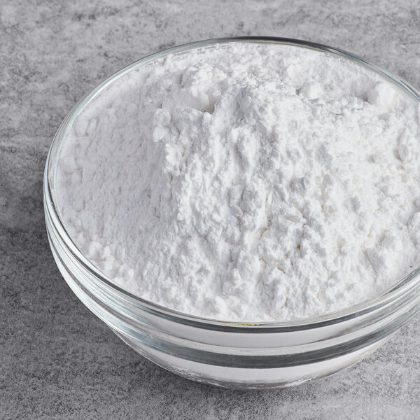 A clear glass bowl filled with white arrowroot starch or flour on a gray surface.