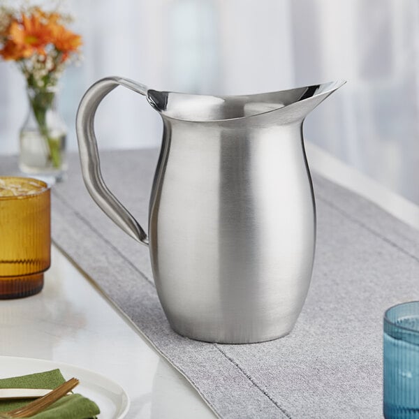 A silver stainless steel Vollrath bell pitcher on a table.