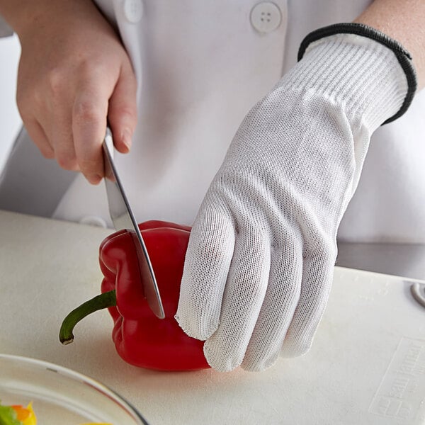 A person wearing MercerGuard white gloves cutting a red pepper on a counter.