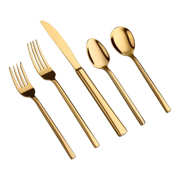 Five pieces of gold-colored flatware, including two forks, a knife, and two spoons, are arranged side by side on a white background.
