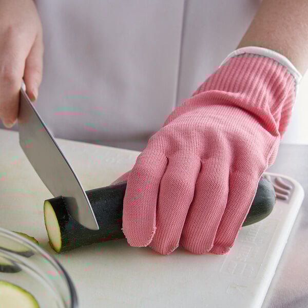 A person wearing pink Mercer Culinary Millennia cut-resistant gloves cutting a zucchini with a knife.