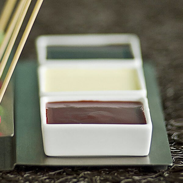 A tray of sauces in white Front of the House square porcelain ramekins.