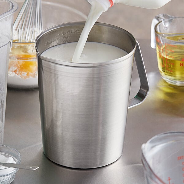 A person pouring milk into a Vollrath stainless steel measuring cup.