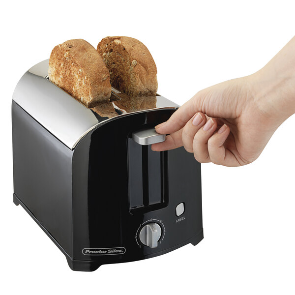 A hand pressing a button on a Proctor Silex toaster with two slices of bread in it.