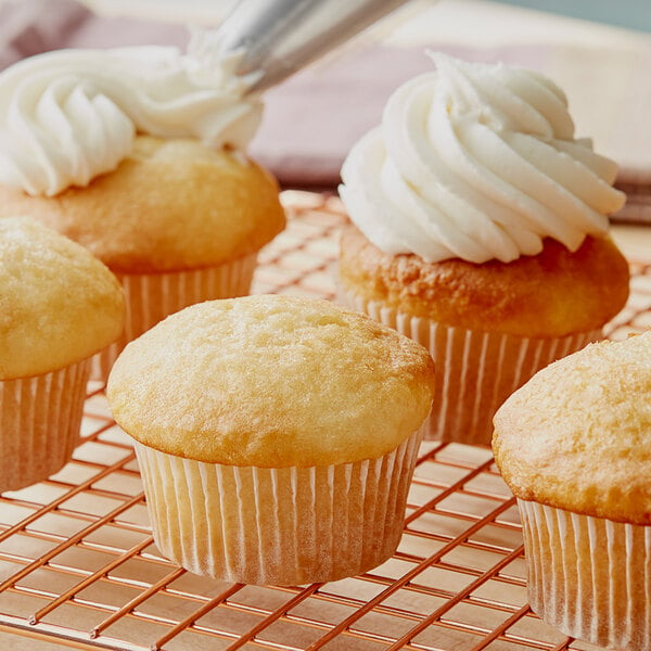 A person using a pastry brush to frost a cupcake with white frosting.