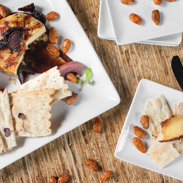 A Front of the House rectangular bright white porcelain plate with a piece of food, nuts, and cheese on it.