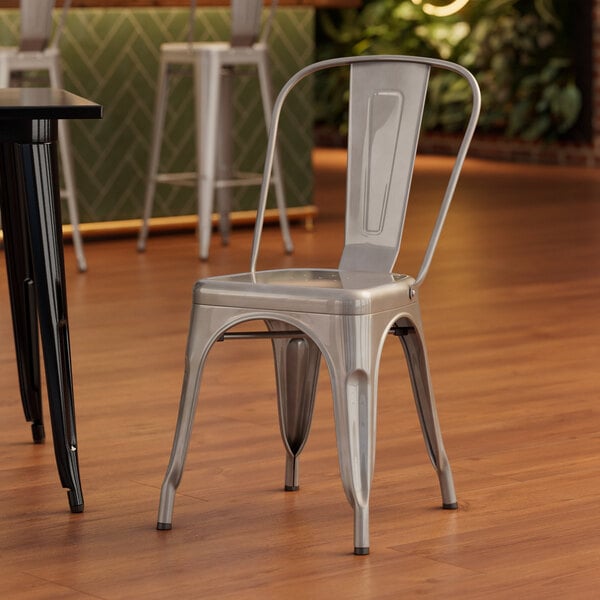 A Lancaster Table & Seating silver metal chair on a wood floor in front of a table.