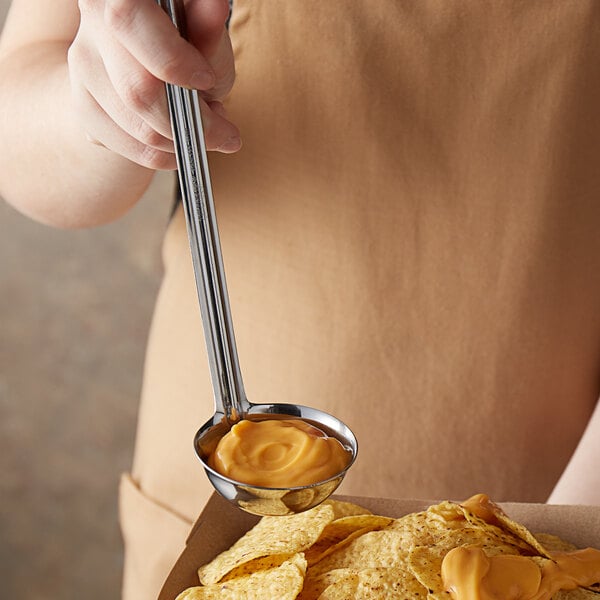 A person holding a Vollrath ladle of cheese sauce.