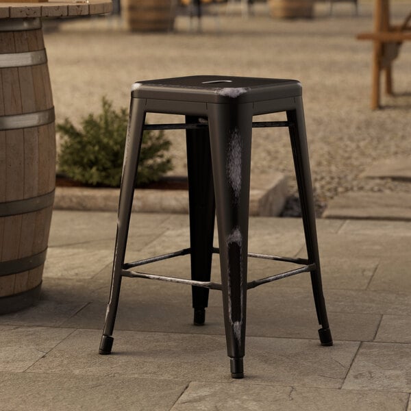 A Lancaster Table & Seating black metal backless counter height stool on a stone surface.