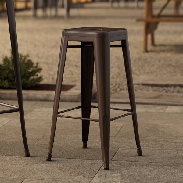 Two Lancaster Table & Seating copper backless barstools on a stone patio.