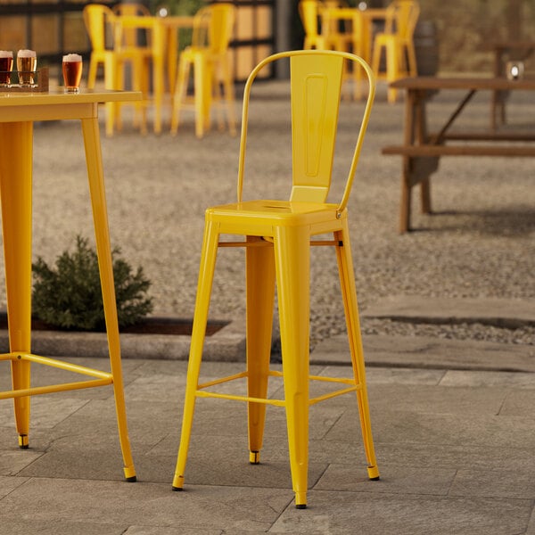 A Lancaster Table & Seating citrine yellow outdoor cafe barstool on an outdoor patio.