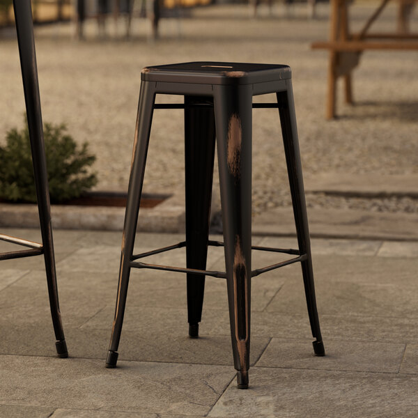 Two Lancaster Table & Seating distressed copper outdoor barstools on a stone patio.