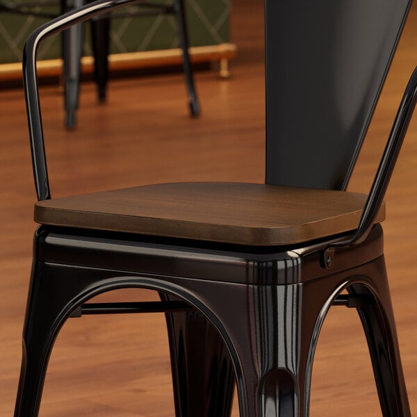 A Lancaster Table & Seating black metal chair with a walnut wood seat.