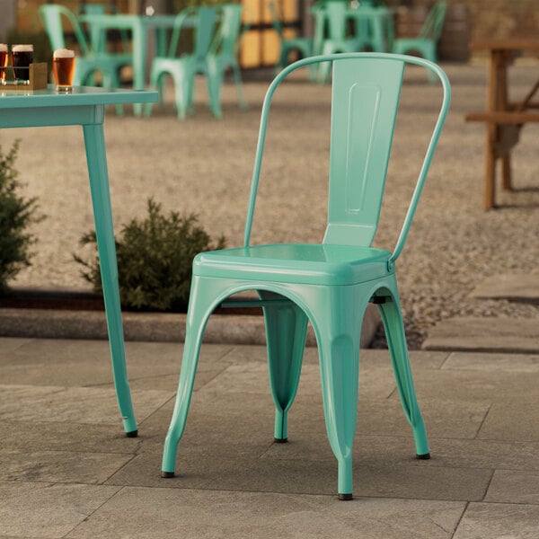 A Lancaster Table & Seating aquamarine metal outdoor cafe chair on a stone patio.