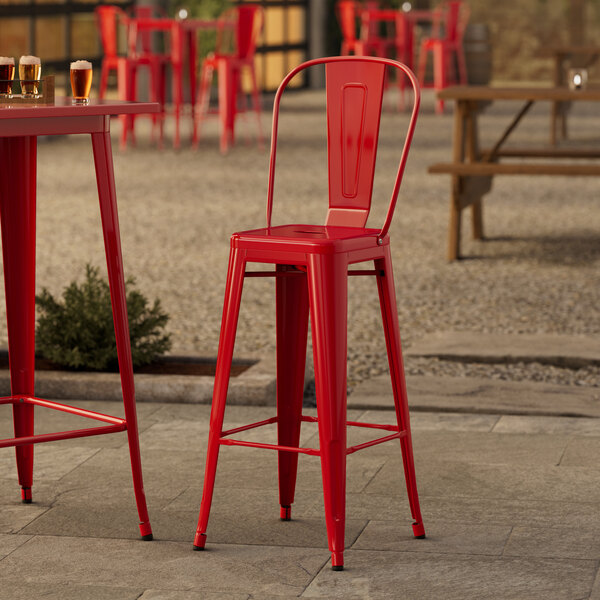 A red metal Lancaster Table & Seating outdoor cafe barstool at a table with beer glasses on it.