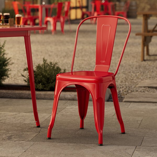 A Lancaster Table & Seating red metal outdoor cafe chair on a stone surface.