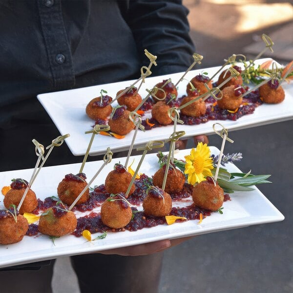 A person holding a Front of the House Kyoto rectangular porcelain plate with meatballs on it.